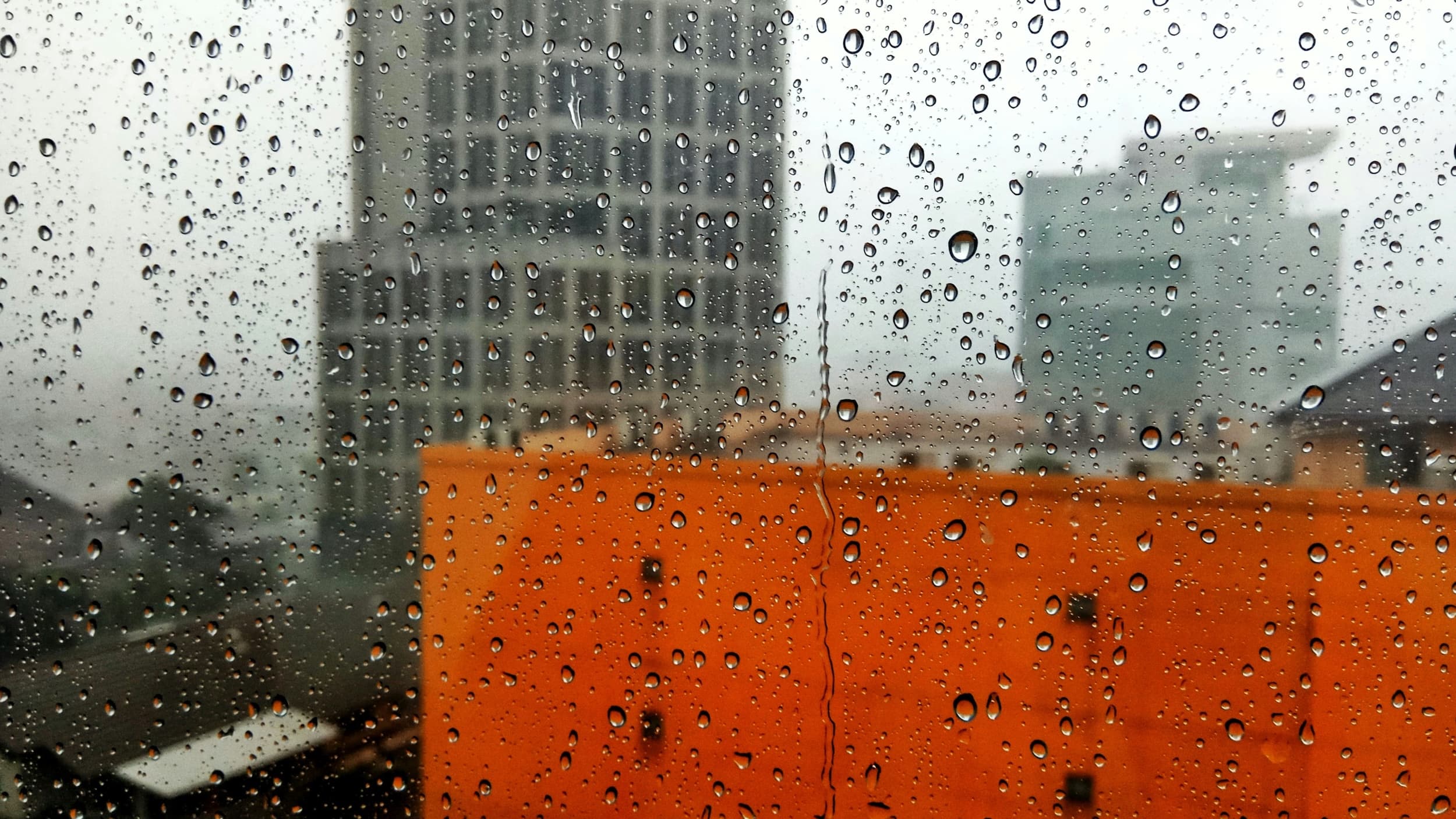 Een raam met regendruppels met in de verte een bouwwerf